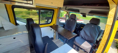 Up-close interior of a yellow custom-built van, showing Carhartt-covered seats and a wooden counter, perfect for an RV rental.
