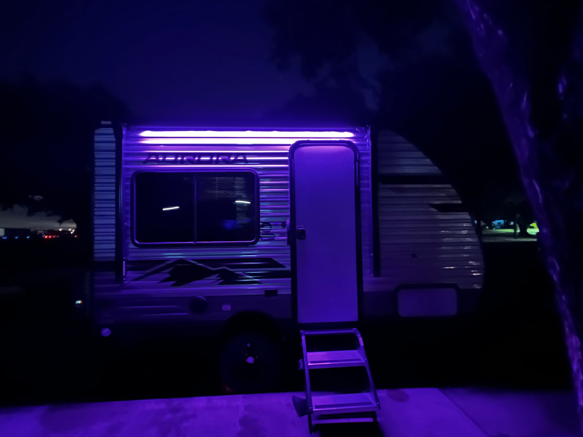 Night view of an RV rental camper with vibrant purple lights illuminating the side, steps, and ground, perfect for an evening setup. — photo 3