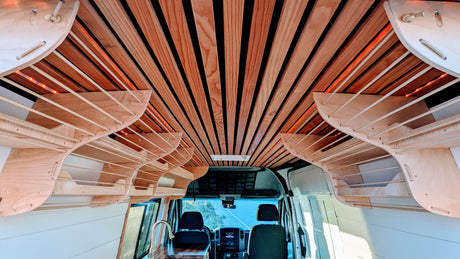 Cozy RV rental camper van interior featuring a slatted wooden ceiling with accent lighting and unique curved overhead storage.
