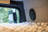 Cozy RV rental interior with a patterned bed, Alpine speaker, and a view of nature from the window.