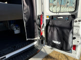 Inside an RV rental: a portable water tank and a Thule storage bag hang on the door, showing mobile living essentials.