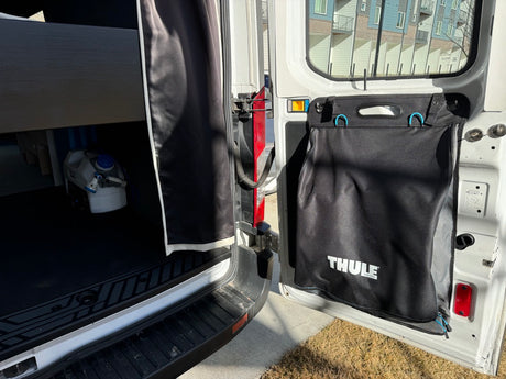 Inside an RV rental: a portable water tank and a Thule storage bag hang on the door, showing mobile living essentials.
