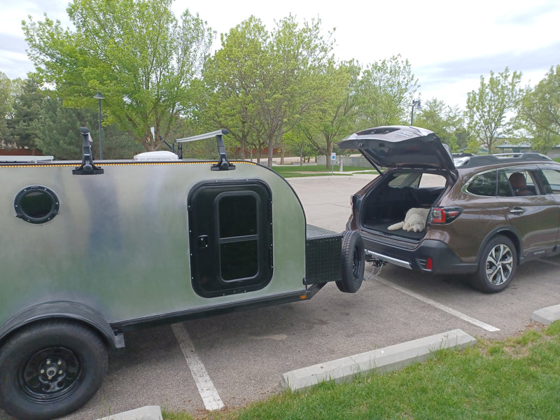 An RV rental teardrop camper is hitched to a Subaru Outback. A white dog rests in the open trunk, ready for travel. — photo 17
