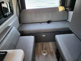 Comfortable RV rental interior featuring grey upholstered seating, wood flooring, and a window with an ocean view.
