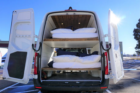 White RV rental van's open rear reveals two cozy bunk beds, showcasing a functional mobile home conversion.