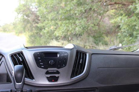 Inside an **rv rental**: dashboard with audio system controls, gear shift, and air vents, overlooking a road and trees.