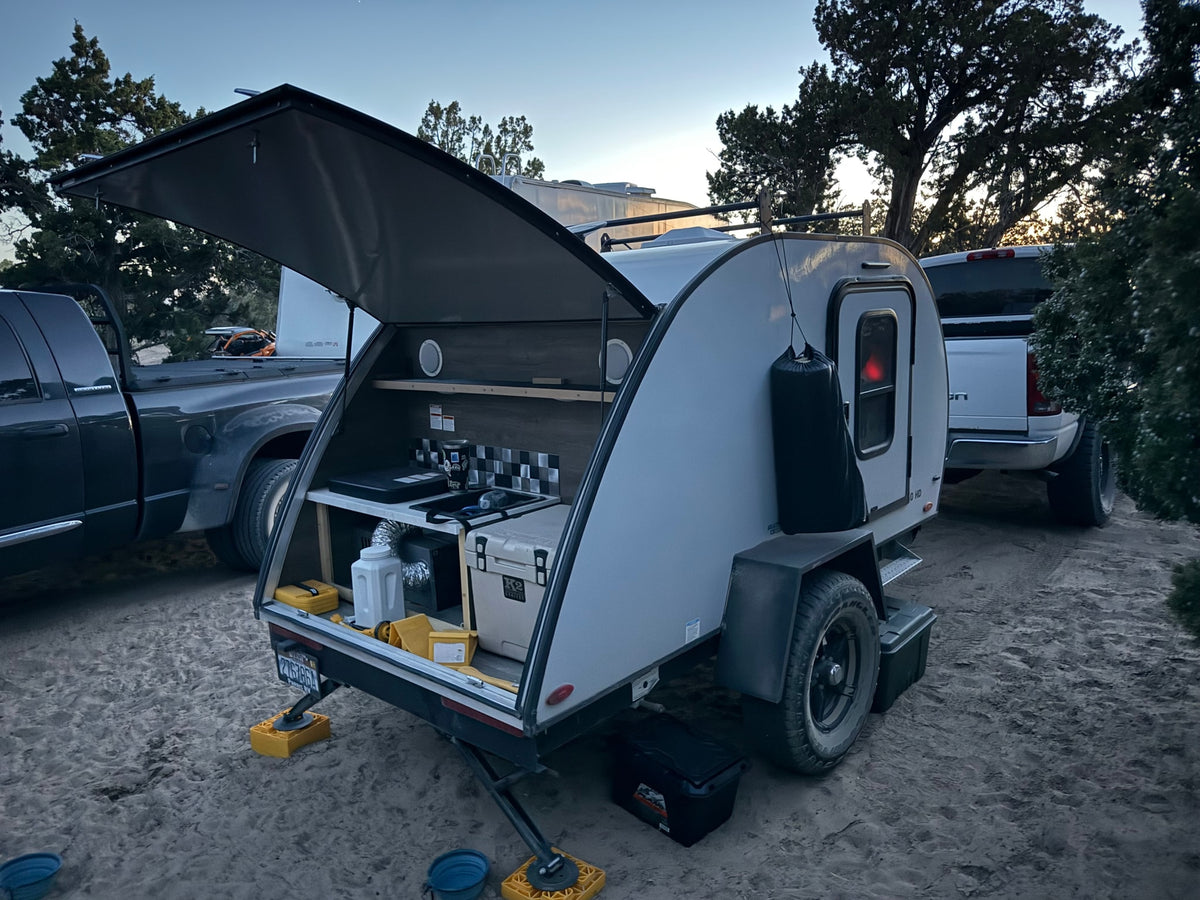 Modern teardrop rv rental camper with an open outdoor kitchen setup, parked on sand alongside a large truck. — photo 8
