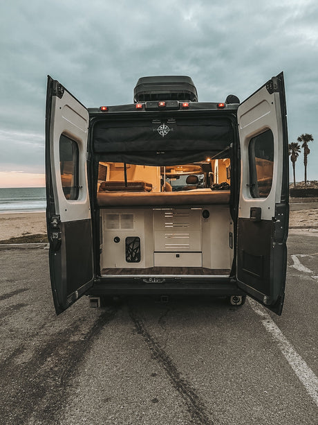 Open doors of this rv rental camper van show a cozy interior at a cloudy beach. Your next travel adventure awaits by the ocean!