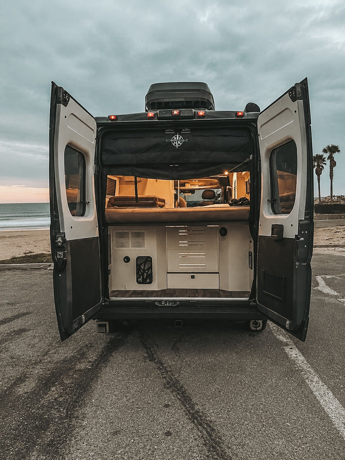 Open doors of this rv rental camper van show a cozy interior at a cloudy beach. Your next travel adventure awaits by the ocean!