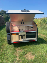 This compact RV rental, a teardrop trailer, features an open rear kitchen with sink, stove, and fridge for outdoor trips.