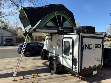 A white travel trailer with an open roof-top tent, ready for an RV rental camping trip, parked in a sunny driveway.
