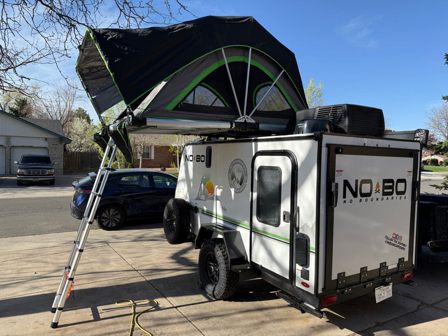 A white travel trailer with an open roof-top tent, ready for an RV rental camping trip, parked in a sunny driveway.