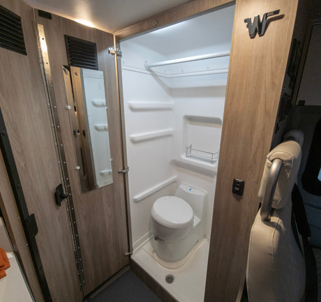 Inside this RV rental, discover a compact bathroom with a bright shower, toilet, and mirror, designed for comfortable journeys.