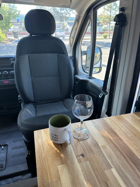 RV rental interior: driver's seat, dashboard, and a wooden table with coffee mug & wine glass. Let the adventure begin!