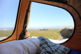 Serene ocean views from a comfortable rooftop tent setup, perfect for your next RV rental road trip. Bed and blanket visible.