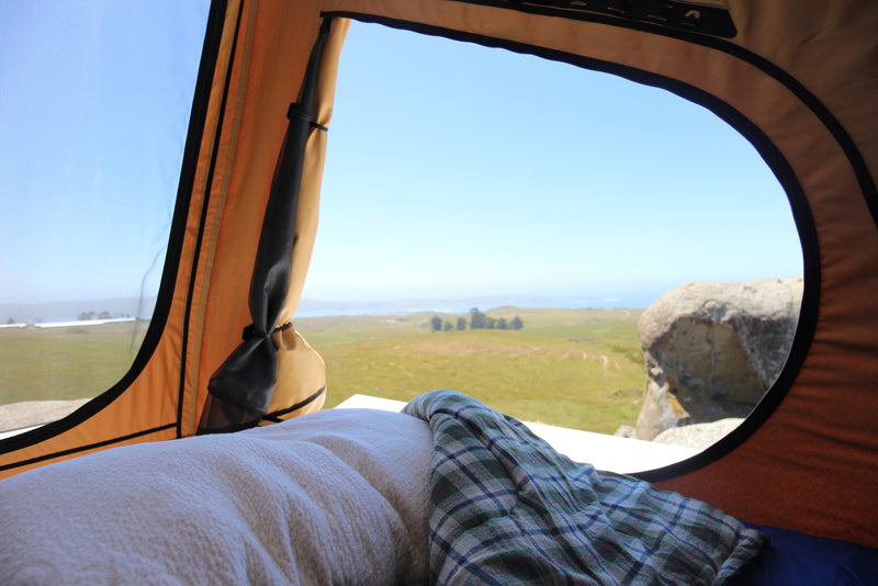 Serene ocean views from a comfortable rooftop tent setup, perfect for your next RV rental road trip. Bed and blanket visible. — photo 8