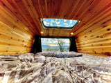 Cozy RV rental interior with bed and wood paneling, offering stunning desert sunset views and a sky through the roof.