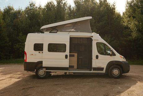 White pop-top camper van for rv rental, parked on dirt road in nature with side door open, revealing interior.