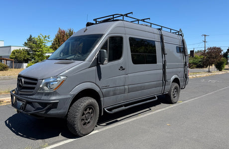 Gray Mercedes-Benz Sprinter adventure van, ready for a rugged rv rental journey. Features roof rack, ladder, off-road tires.