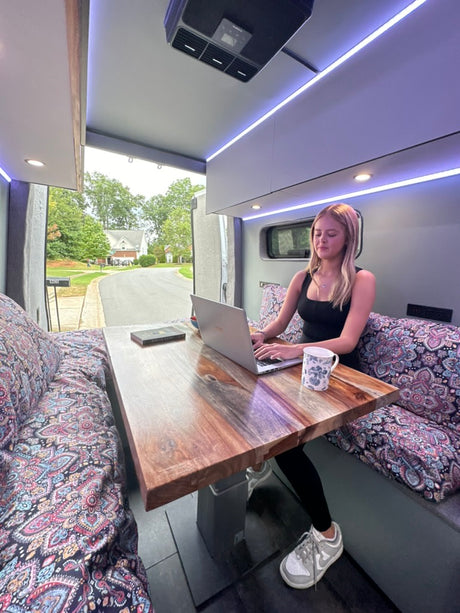 Enjoy remote work from your RV rental! This modern camper van features a cozy dinette, laptop, and scenic views.