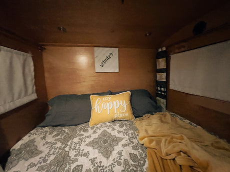Cozy RV rental bedroom with a comfy bed, "my happy place" pillow, and "wander" sign for comfortable travel.