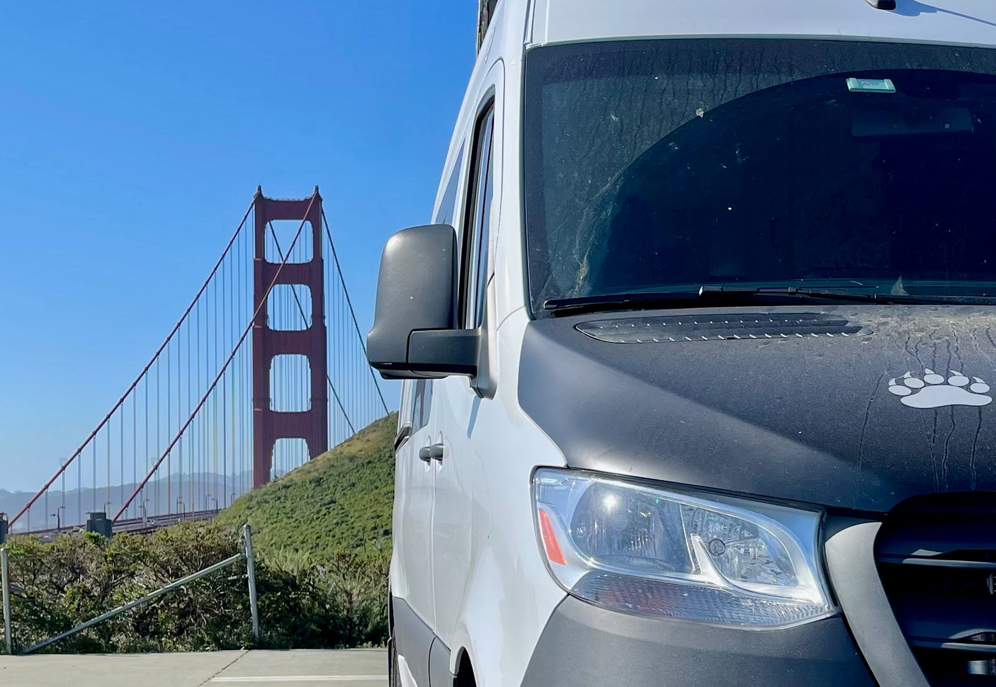 White RV rental van facing Golden Gate Bridge in San Francisco. Ready for your next travel adventure under a clear sky.