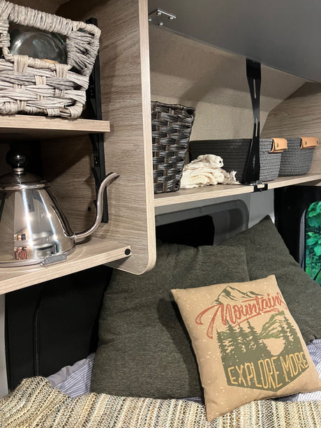 RV rental showing organized shelves, baskets, a kettle, and a cozy bed with an "Explore More" pillow.
