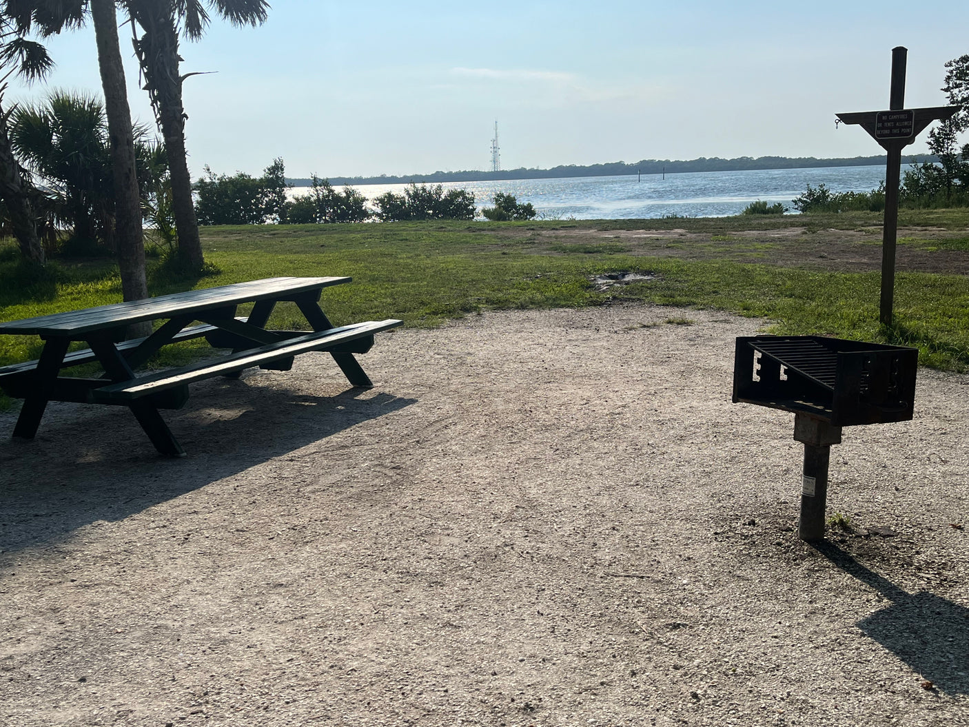 RV rental friendly: waterfront picnic area with a grill & table in a tranquil park setting, perfect for outdoors.