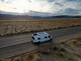 Scenic desert road trip with an rv rental. White camper van parked by mountains under a vast, cloudy sky.