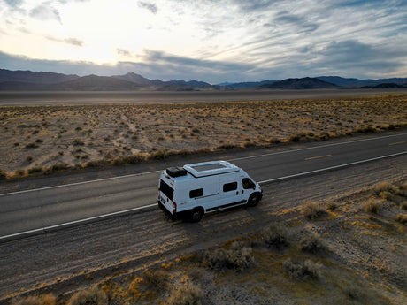 Scenic desert road trip with an rv rental. White camper van parked by mountains under a vast, cloudy sky.