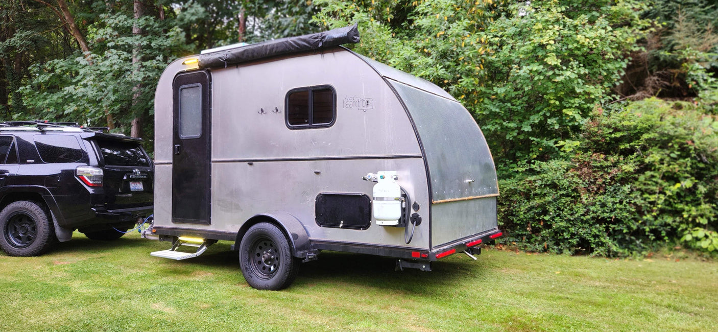 A silver teardrop camper, hitched to a black SUV and parked on green grass, is ideal for an rv rental.