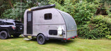 A silver teardrop camper, hitched to a black SUV and parked on green grass, is ideal for an rv rental.
