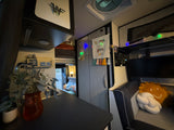 This RV rental's cozy interior features a compact kitchen, an upper sleeping bunk, and a comfy lounge with a TV and decor.