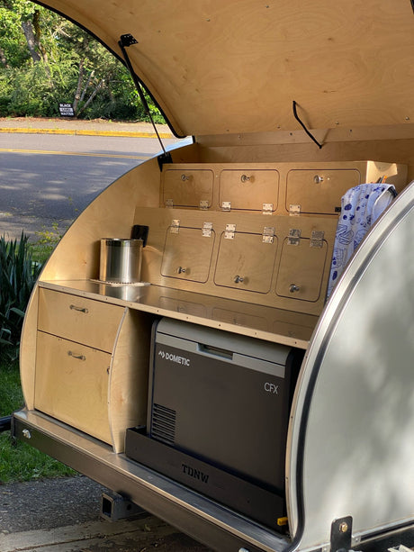 This RV rental teardrop camper reveals its open rear galley kitchen, featuring a Dometic cooler, drawers, and ample storage cabinets.