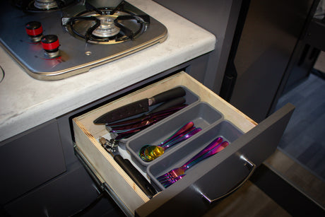 RV rental kitchen featuring an open drawer with vibrant iridescent cutlery and knives next to a compact two-burner stove.