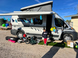 A boy celebrates his birthday by a pop-top RV rental, decorated with tassels, balloons, and gifts in a desert setting.