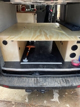 Camper van interior for rv rental with custom wooden bed platform, storage, and E-track floor in the rear.