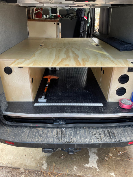 Camper van interior for rv rental with custom wooden bed platform, storage, and E-track floor in the rear.