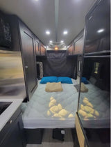 Inside a modern rv rental, showing a comfortable bed, overhead cabinets, and a compact kitchenette setup.