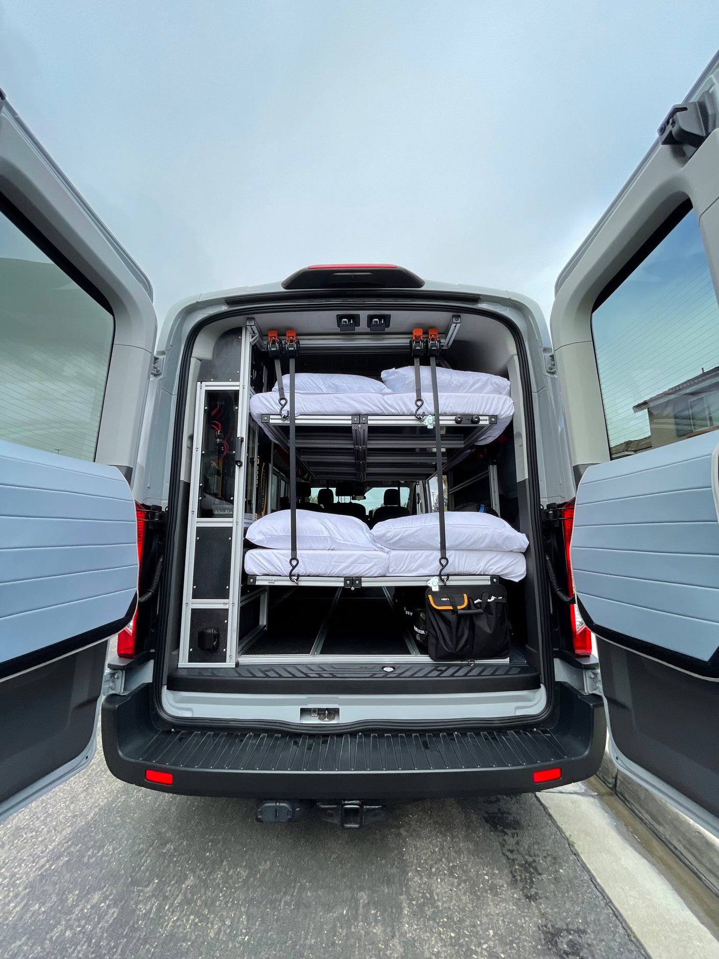 Rear view of a grey van converted for RV rental, featuring a custom interior with two stacked bunks & storage solutions.
