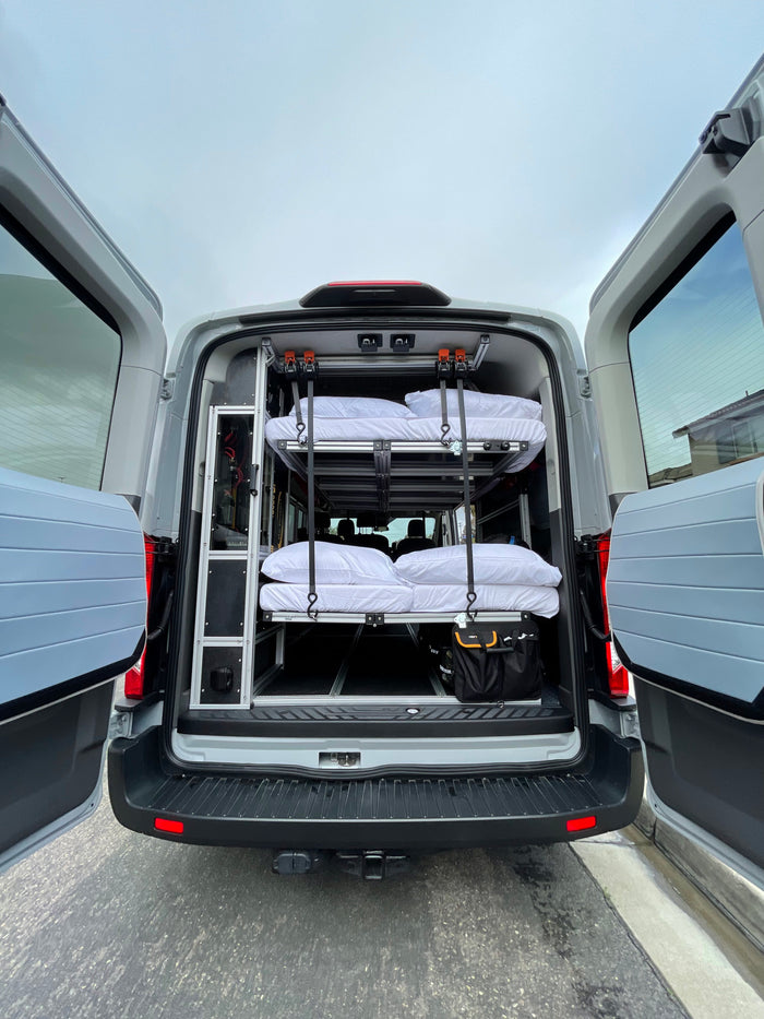 Rear view of a grey van converted for RV rental, featuring a custom interior with two stacked bunks & storage solutions.