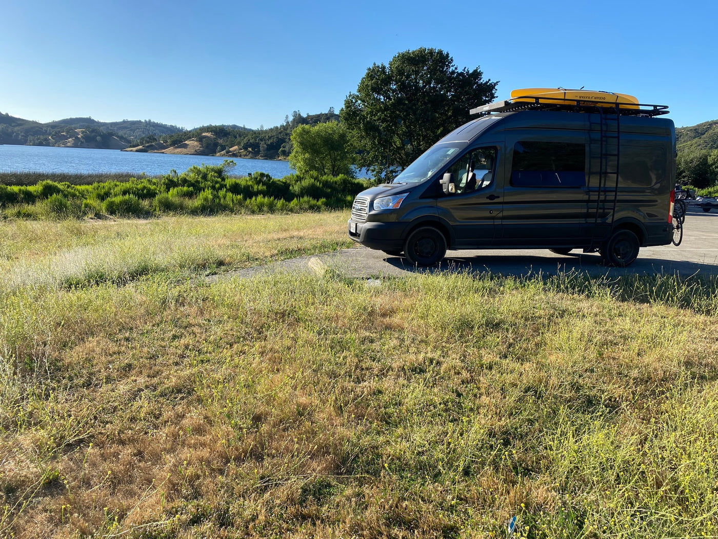 Adventure-ready RV rental: dark grey camper van with kayak & bike rack by a scenic lake & hills. — photo 20