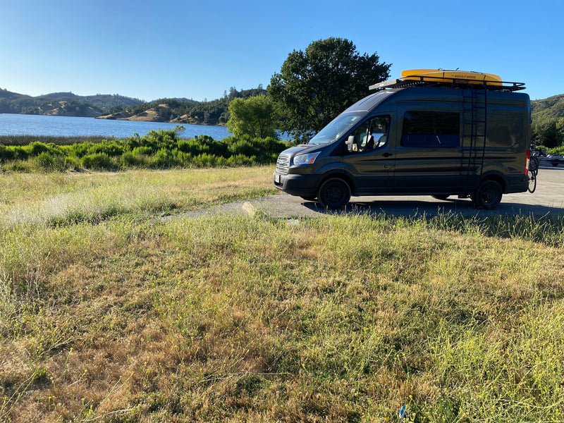 Adventure-ready RV rental: dark grey camper van with kayak & bike rack by a scenic lake & hills. — photo 40