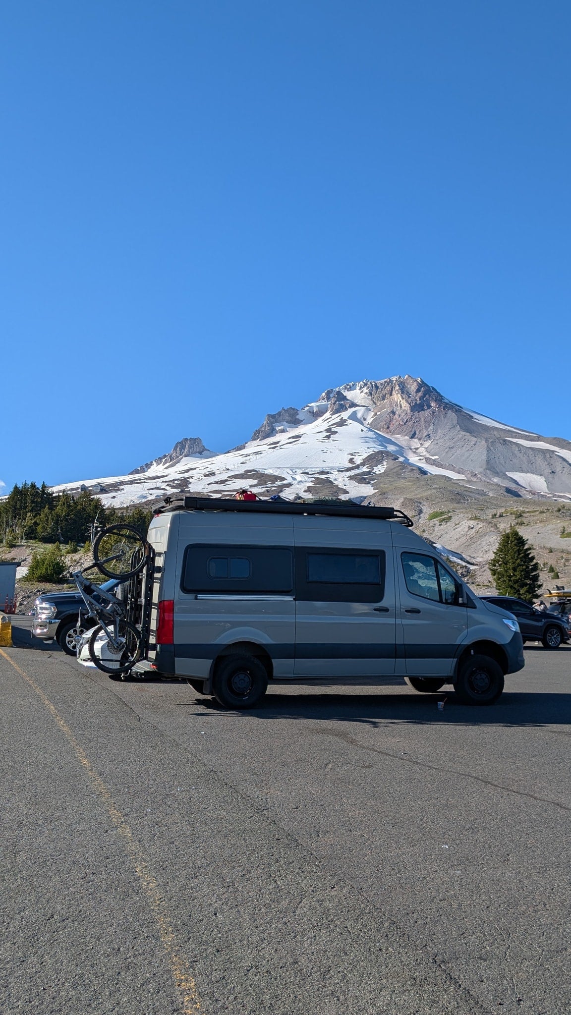 This gray camper van, perfect for an RV rental adventure, is parked with a bike rack against a stunning snow-capped mountain. — photo 12