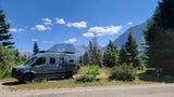 A gray Winnebago Revel RV rental parked at a scenic mountain campsite. Family enjoys the peaceful outdoor view.
