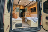 Step inside this cozy RV rental camper van, featuring a custom interior with beds, a table, and kitchen for your next adventure.