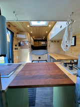Spacious, wood-paneled camper van interior shows kitchen, bed, and skylight. An excellent option for rv rental adventures.