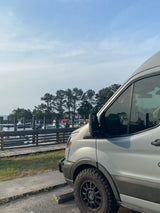 RV rental van beside a serene boat dock, showing its robust tires and the peaceful waterfront scene.