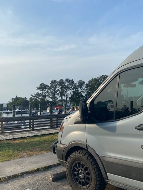 RV rental van beside a serene boat dock, showing its robust tires and the peaceful waterfront scene.