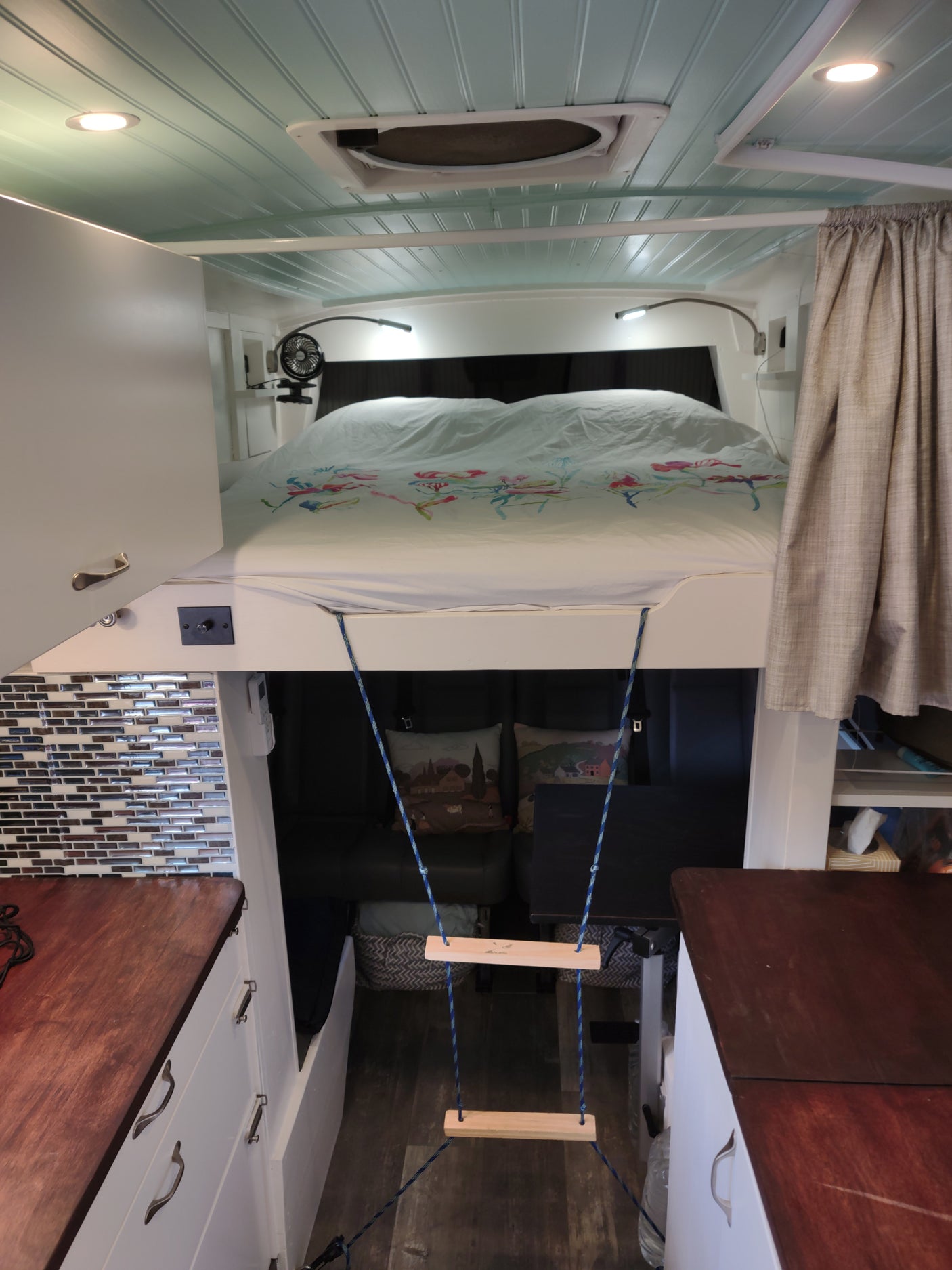 Cozy rv rental interior features a loft bed with rope ladder above dining, light blue ceiling, and compact kitchen.